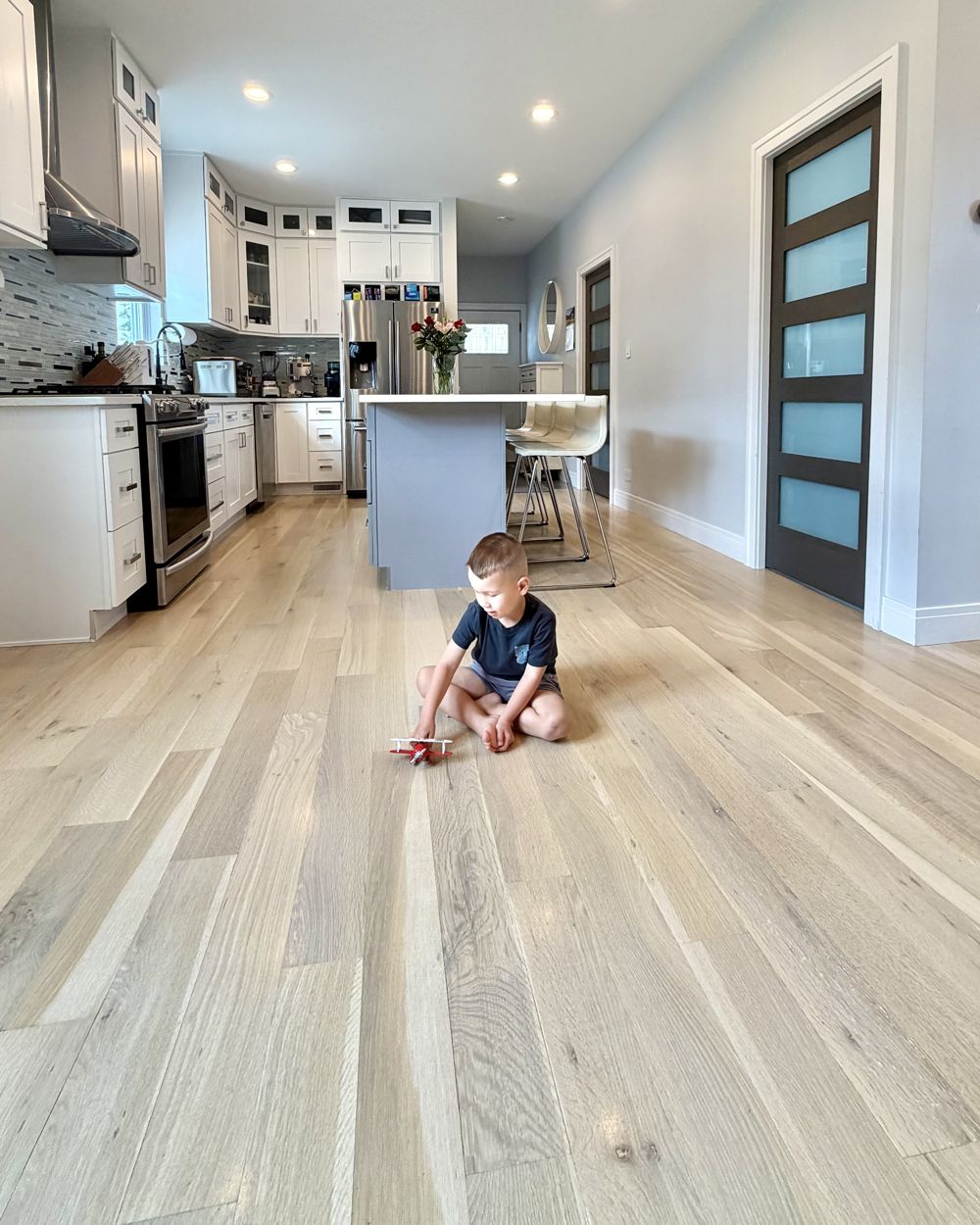 Little boy playing with a toy airplane on freshly refinished hardwood floors in a bright Chicagoland living room